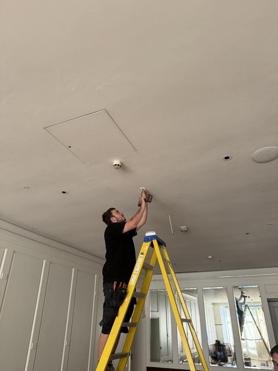 Fitz engineer on a ladder fitting a smoke detector to the ceiling of a period property